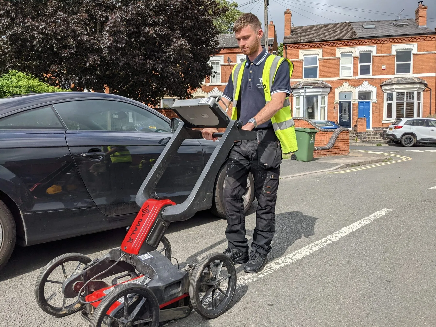 Technician pushing a ground-penetrating radar unit along a residential street